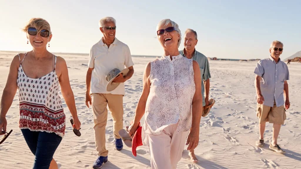 Groupe de seniors marchant sur la plage en riant